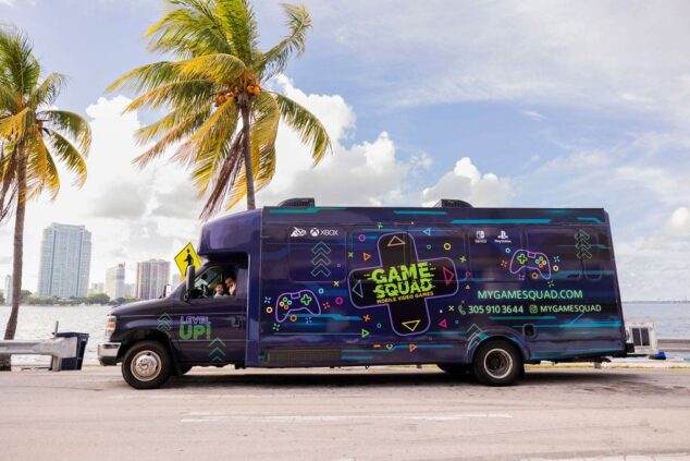 Kids of mixed ages playing on PS5 and Xbox inside an air-conditioned My Game Squad video game truck at a Miami neighborhood event