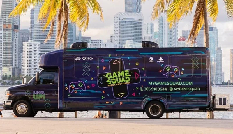 The My Game Squad gaming bus parked by the bay with the Miami skyline behind it